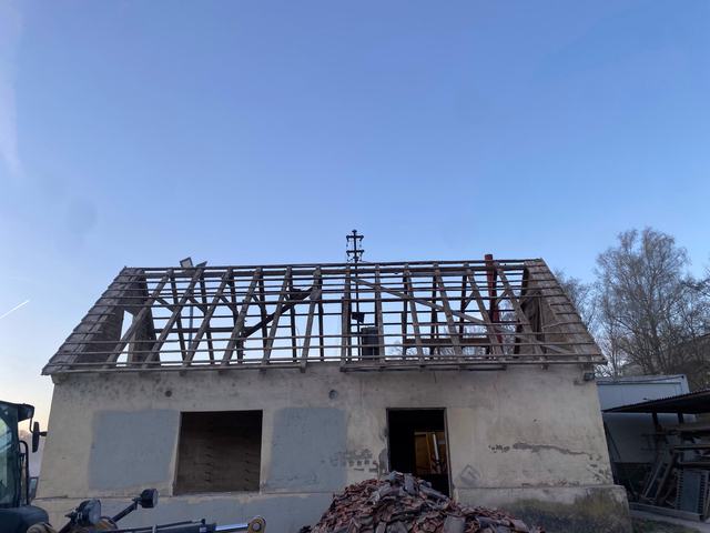Haus mit abgedecktem Dach, vom Dach steht nur noch der Dachstuhl, davor ein Haufen alter Dachziegel