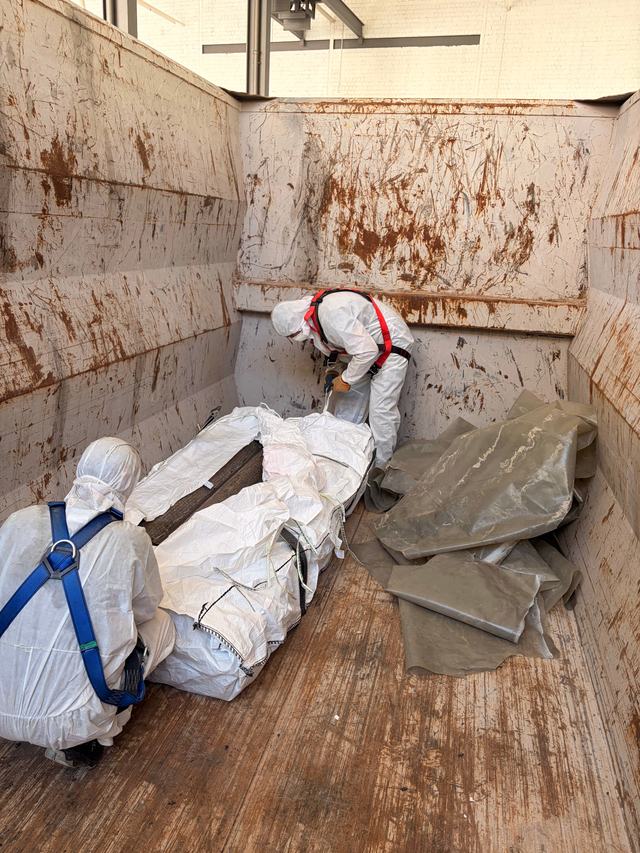 Zwei Mitarbeiter in Schutzanzügen verladen Big Bags in einen Container