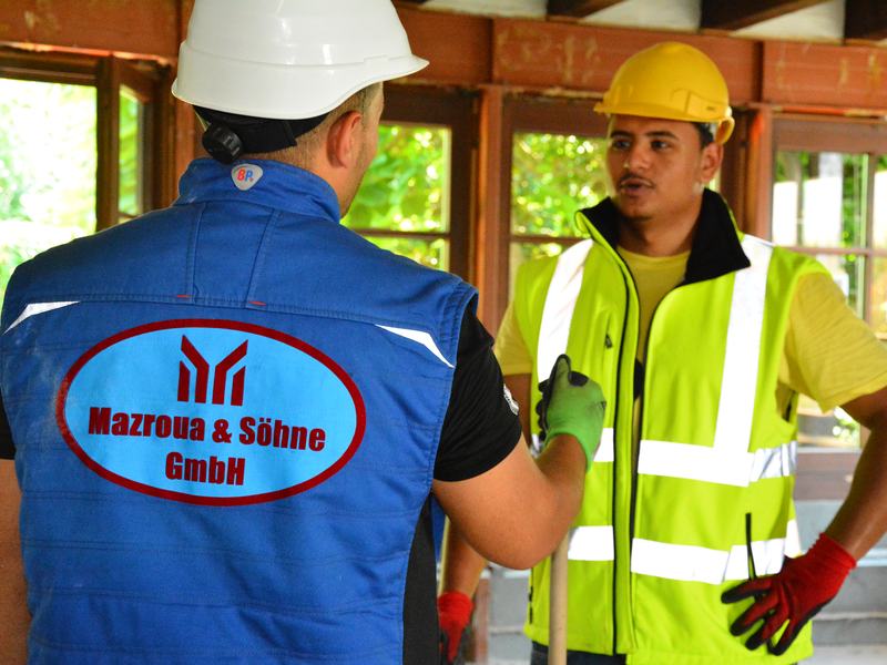 Mitarbeiter in Firmenweste mit dem Logo von Mazroua & Söhne im Gespräch auf der Baustelle